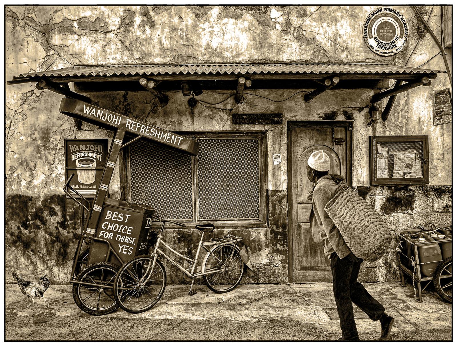 man with straw bag on his bak waling in front a shop.