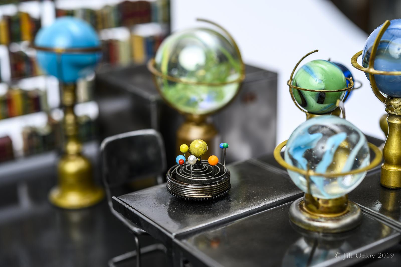 A detail of a larger sculpture showing the miniature orrery model of the solar system and several globes made of marbles within a scene of the movie Wings of Desire