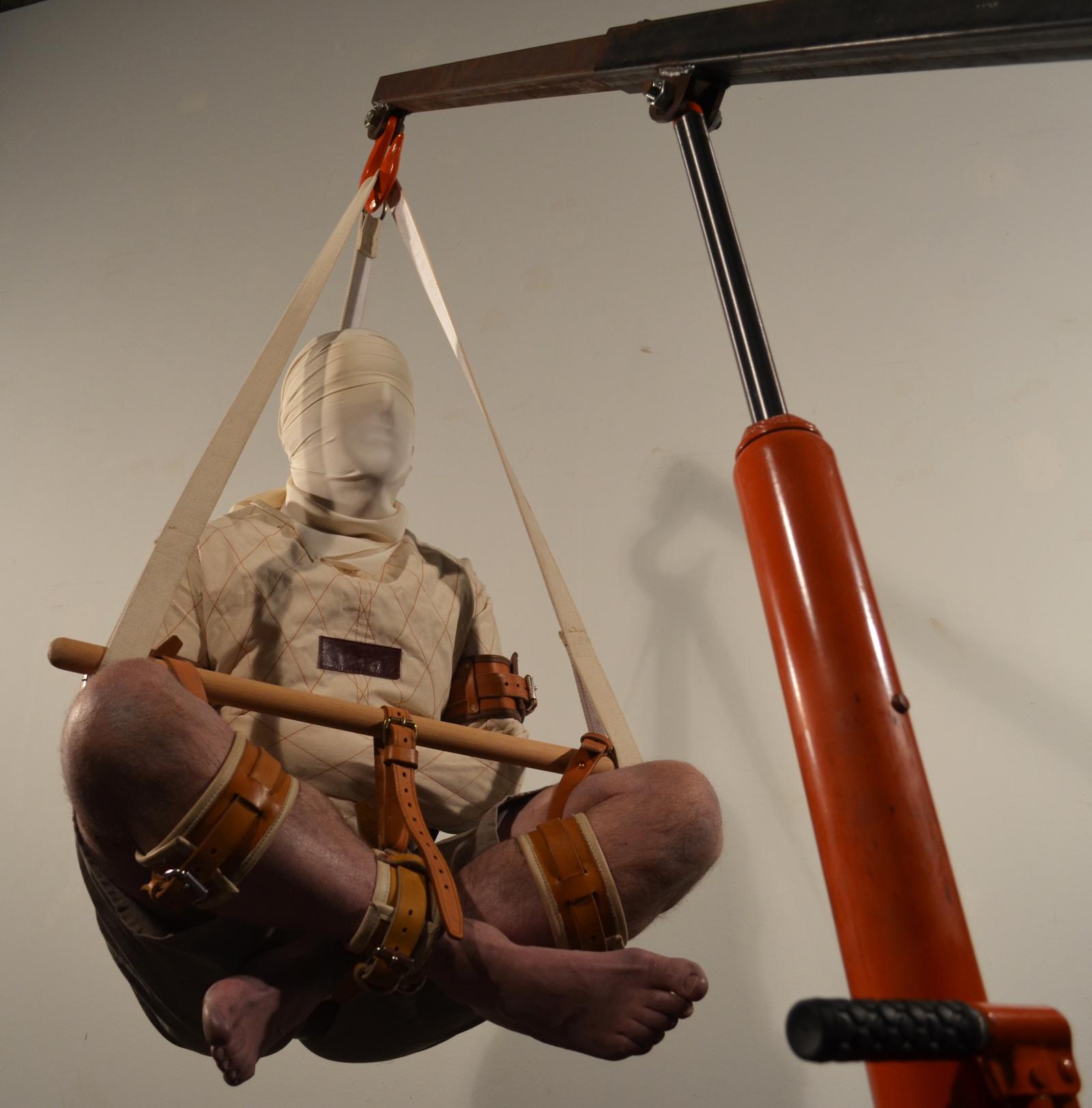 Subject (me) hoisted, about to be lowered into bag
As my work became more complex with multiple participants, my role in the performances changed from subject to orchestrator, I wanted to get back to a simple act where I would be the person facing the dilemma.
Compound Balance consists of 2 sturdy bags. One contains a bound person and the other, a counterweight filled with sand that escapes in a slow trickle from a funnel in the bottom of the bag. Both bags are suspended by a balance mechanism with a lever mechanism that favours the counterweight bag. The bag containing the person closed by a scissor mechanism that stays locked under tension. As long as there is sufficient mass in the counterweight, the person remains locked and suspended in the bag and must wait for enough sand to escape in order to equalize the weight and release the lock.
