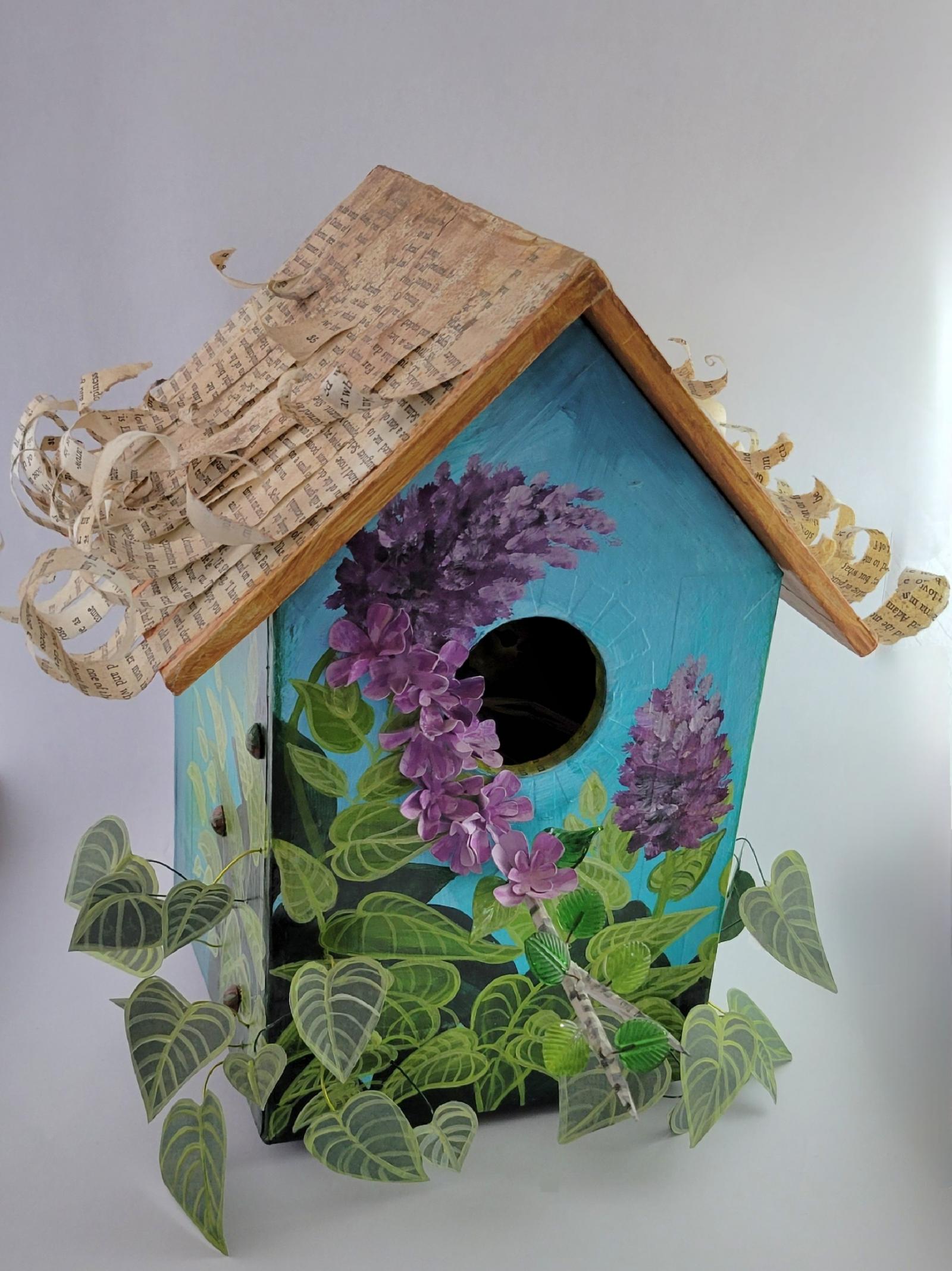 This mixed media piece was created from cast-off materials - shipping boxes, old books, scrapbook paper, beads etc. The roof can be removed to view inside where a paper clay bird watches over her precious eggs. Various symbology is present in the piece. On the back of the pieces is a night sky with a bird constellation. There is a removable stand (not shown) made from a tree limb where a poem about birds is inscribed.
