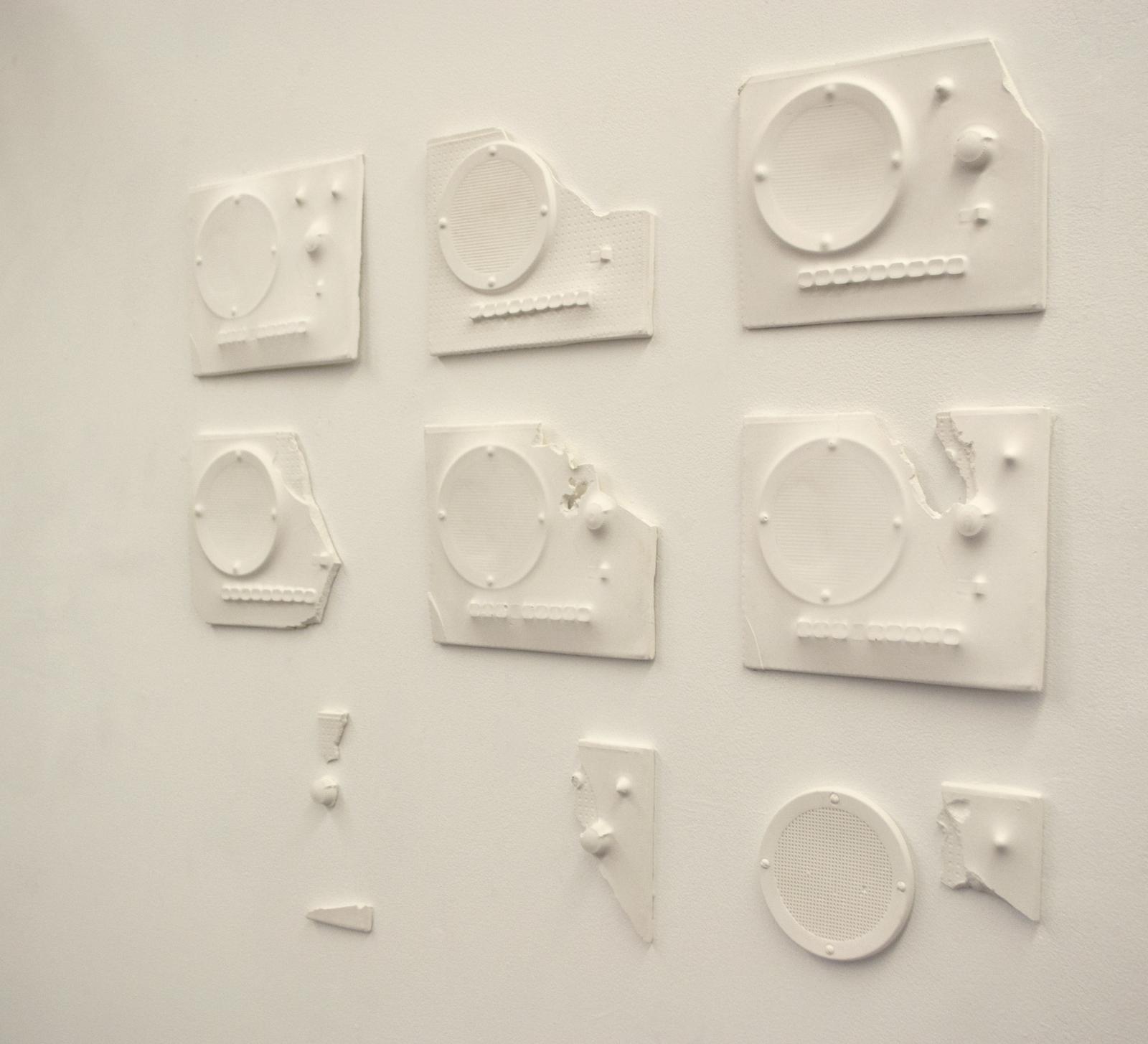 Ghost Comms is a meditation on the intercoms within the rooms of my New York home. They have been present as long as I've lived there but were never functional. While I grow, coming and going from home, they sit static and absorb the chaos, loudness, and silence of a one-floor home to seven people. Over the years, they have come to mean more to me about communication and lack thereof.
This piece is composed of plaster casts of the original systems I dismantled from the walls of my house. Each mold yielded a different intercom cast, broken and layered with texture in different ways. The repetitive nature and eventual disappearance of most of the intercom face is a reflection of the passage of time.
