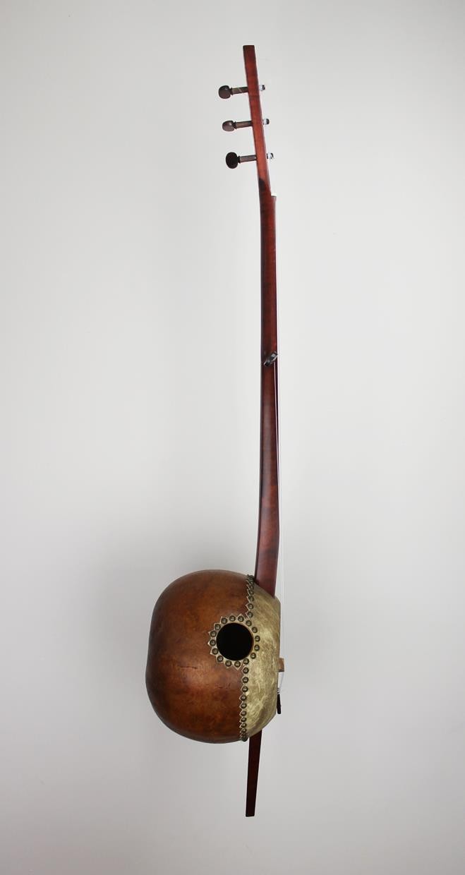 Neck cut from raw maple, stained, finished and fit to gourd. Gourd cut open, cleaned out and prepared for goat-skin soundboard. Goatskin soaked and stretched over opening in gourd. Strings stretched from handmade tailpiece, over bridge, nut and to tuni