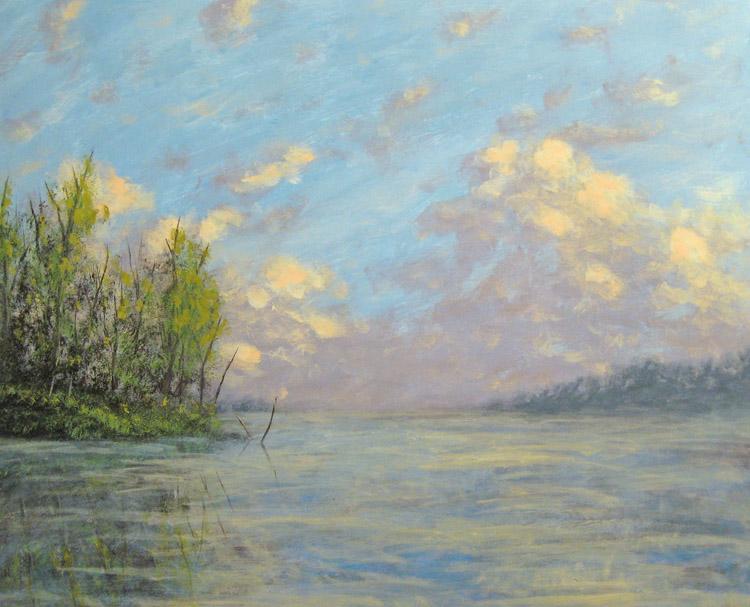 Low evening sunlight stretches across a vast lake, catching the shores and tree tops in a warm glow. Miles away, storm clouds are illuminated in the waning light of day.
