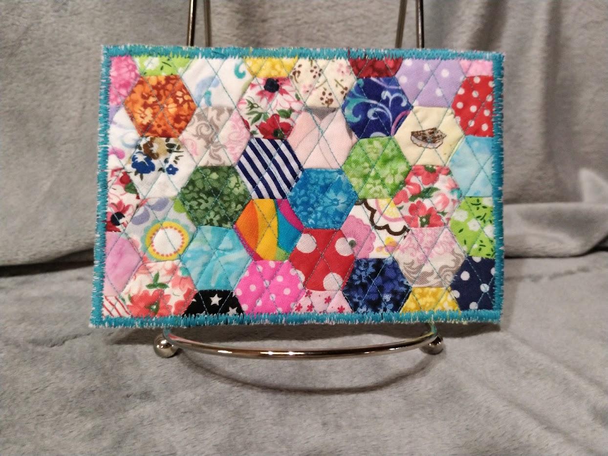 Handsewn hexagons, machine quilted piece, appliqued onto cardstock to be used as an actual postcard and then can be framed in a 4x6 frame as a keepsake. Cotton fabrics, thread, cardstock, envelope.